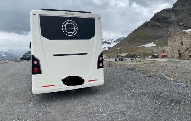 Camping-car vu de l'arrière avec en fond une montagne enneigée et un ciel nuageux